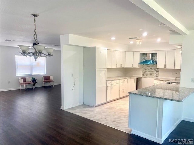 kitchen featuring white cabinetry, wall chimney range hood, decorative backsplash, sink, and a chandelier