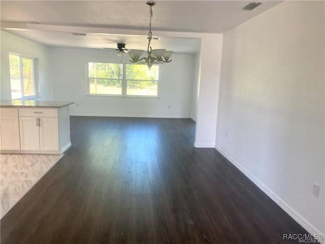 unfurnished dining area with ceiling fan with notable chandelier, a wealth of natural light, and dark hardwood / wood-style floors