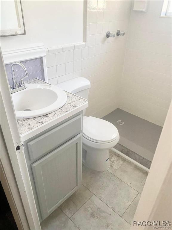 bathroom with toilet, vanity, tile walls, and tiled shower