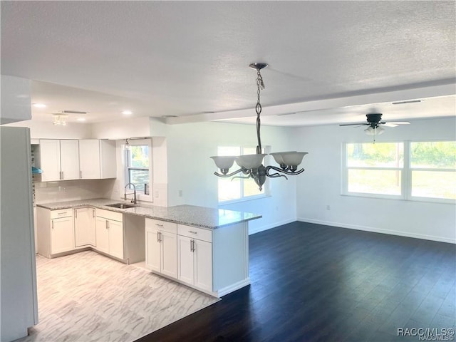 kitchen with ceiling fan with notable chandelier, white cabinets, light hardwood / wood-style floors, sink, and light stone counters