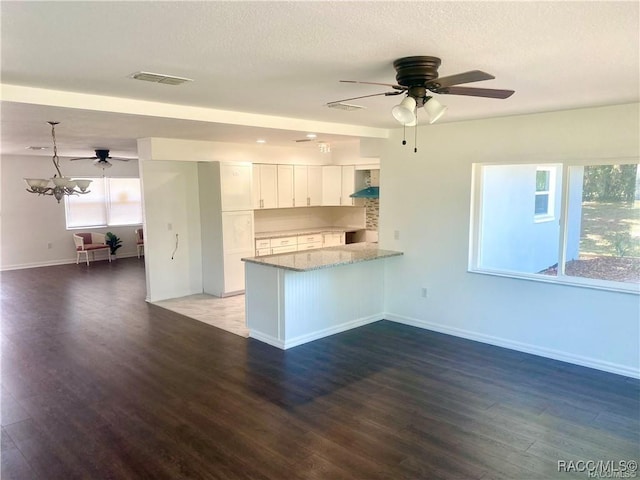 kitchen with white cabinetry, kitchen peninsula, light stone countertops, a chandelier, and wall chimney exhaust hood