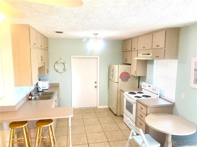 kitchen featuring a textured ceiling, light tile patterned flooring, light brown cabinetry, and white appliances