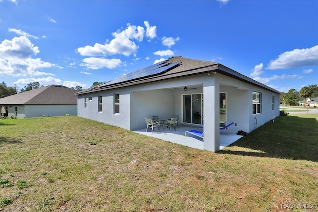 back of property with solar panels, a patio area, and a lawn