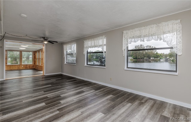 spare room with a textured ceiling, dark hardwood / wood-style flooring, a water view, and ceiling fan