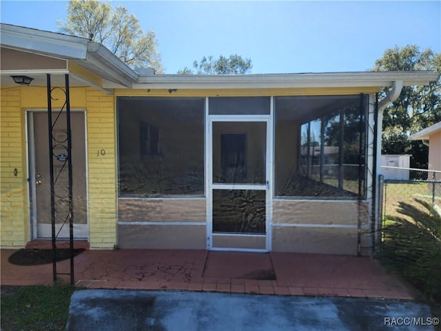 back of property featuring brick siding, a sunroom, and fence