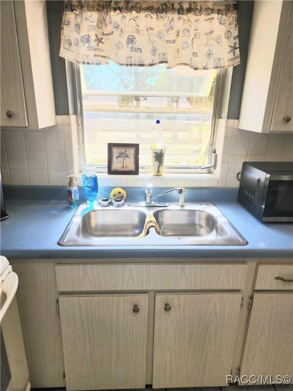 kitchen featuring a sink, stove, backsplash, and light brown cabinetry