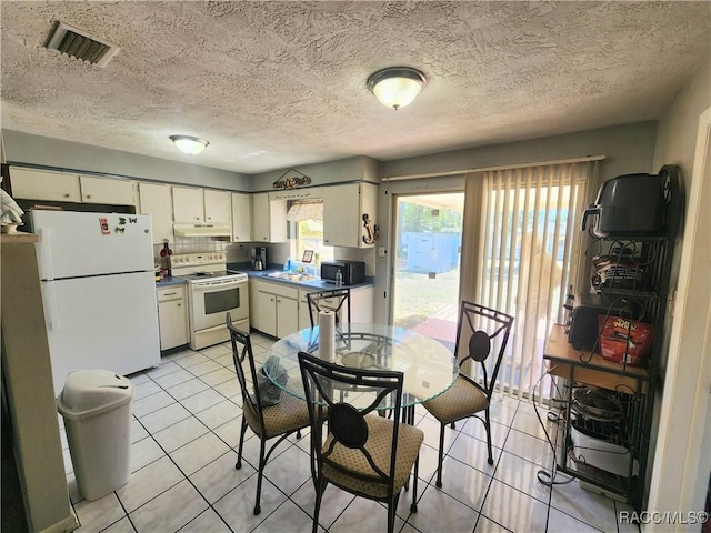 kitchen featuring white appliances, visible vents, light tile patterned flooring, a sink, and under cabinet range hood