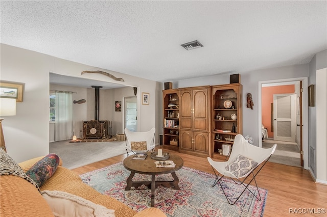 living room with a textured ceiling, light wood-type flooring, and a wood stove