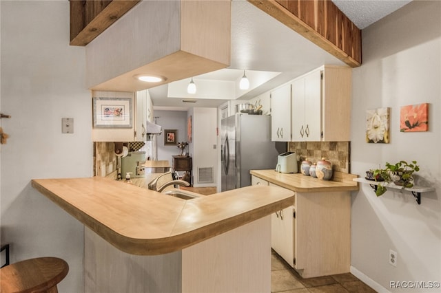 kitchen with kitchen peninsula, stainless steel fridge, backsplash, and light tile patterned floors