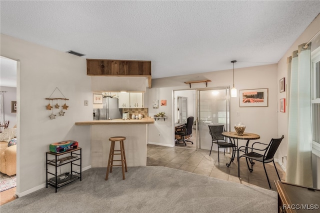 kitchen featuring carpet, a kitchen breakfast bar, stainless steel refrigerator with ice dispenser, decorative light fixtures, and kitchen peninsula