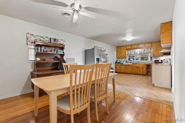 dining room with baseboards, light wood finished floors, visible vents, and a ceiling fan