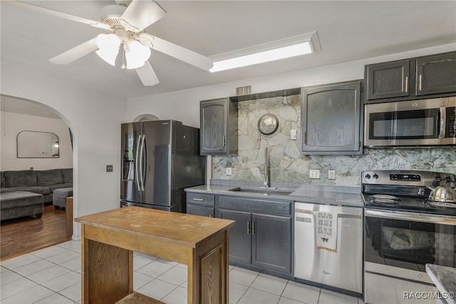 kitchen featuring a sink, tasteful backsplash, arched walkways, appliances with stainless steel finishes, and light tile patterned floors