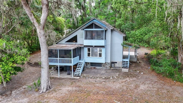 back of house with stairway, a view of trees, and a sunroom