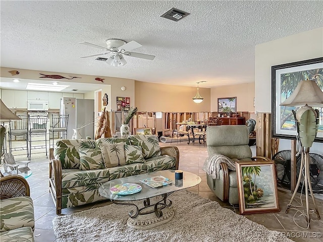 living area featuring a ceiling fan, a textured ceiling, visible vents, and light tile patterned floors