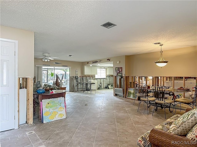 tiled living area featuring visible vents, a ceiling fan, and a textured ceiling