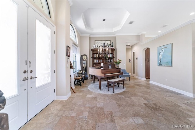 foyer entrance with an inviting chandelier, ornamental molding, and a tray ceiling