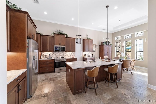 kitchen with light stone counters, a kitchen breakfast bar, pendant lighting, stainless steel appliances, and a kitchen island with sink