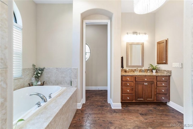 bathroom with hardwood / wood-style flooring, vanity, and tiled bath