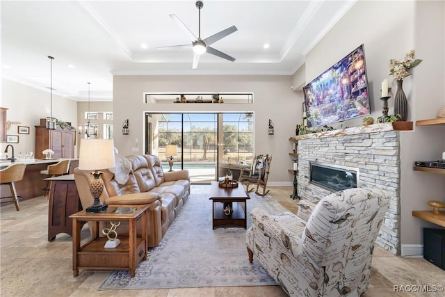 living room with ceiling fan, ornamental molding, a tray ceiling, and a fireplace