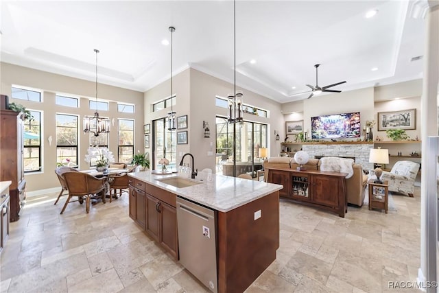 kitchen with sink, hanging light fixtures, stainless steel dishwasher, a raised ceiling, and an island with sink