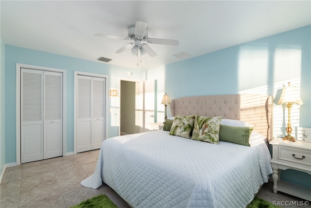 tiled bedroom with multiple windows, ceiling fan, and two closets