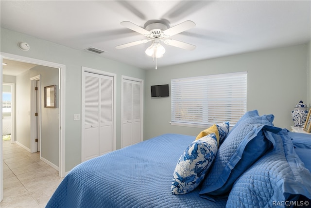 tiled bedroom with ceiling fan and two closets