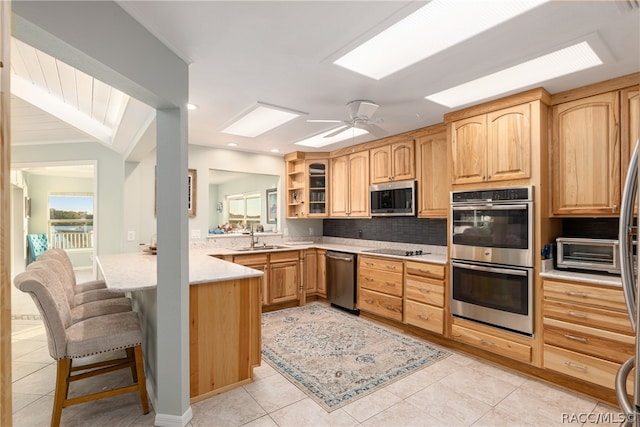 kitchen featuring ceiling fan, sink, stainless steel appliances, a breakfast bar area, and light tile patterned flooring