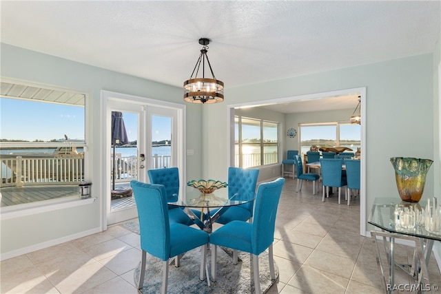 tiled dining room with french doors, a water view, and a notable chandelier