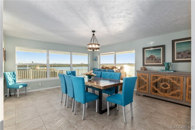 tiled dining area with a textured ceiling, a water view, and an inviting chandelier