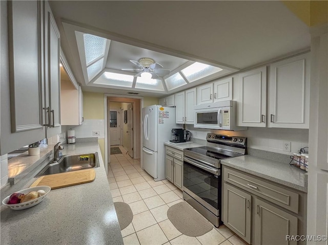 kitchen with a skylight, light tile patterned floors, light countertops, a sink, and white appliances