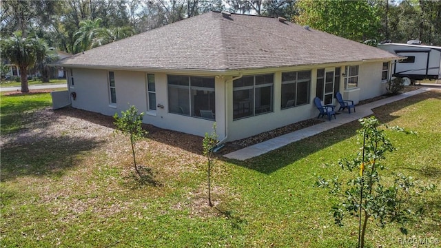 rear view of house featuring roof with shingles, a lawn, a sunroom, and stucco siding