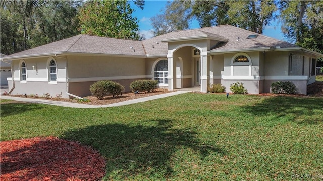 view of front of home featuring a shingled roof, a front yard, and stucco siding