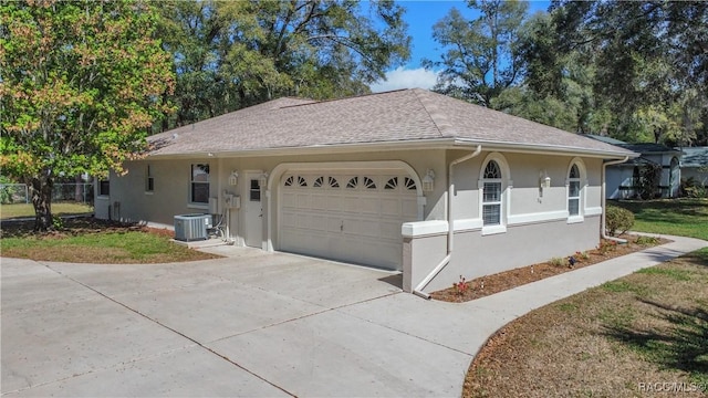 ranch-style house with driveway, an attached garage, central AC, and stucco siding