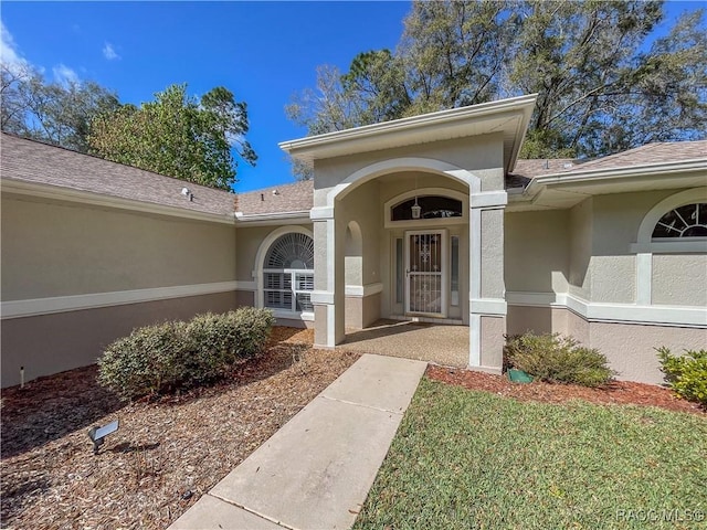 view of exterior entry with a yard and stucco siding