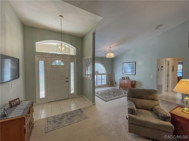 foyer with light tile patterned floors, high vaulted ceiling, a chandelier, light carpet, and visible vents