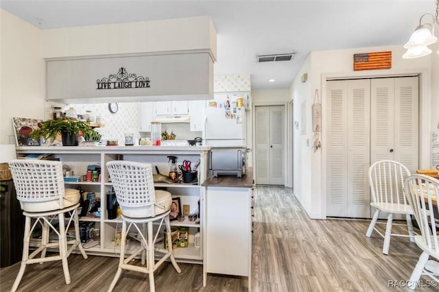 bar with white fridge, backsplash, decorative light fixtures, white cabinets, and light hardwood / wood-style flooring