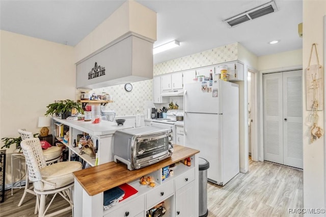 kitchen with white fridge, light hardwood / wood-style floors, backsplash, and white cabinets