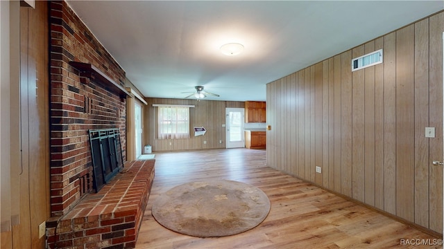 living room with light wood-type flooring, a brick fireplace, ceiling fan, and wooden walls