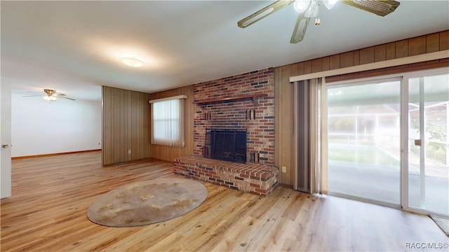 unfurnished living room with light hardwood / wood-style floors, a fireplace, and wooden walls