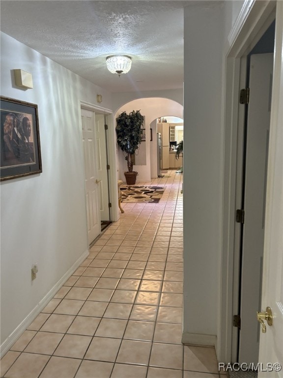 hall with arched walkways, light tile patterned floors, and a textured ceiling
