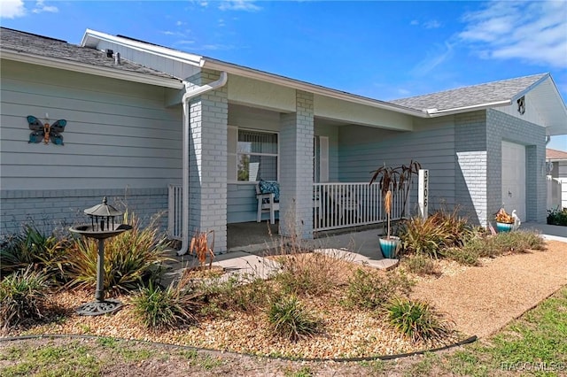 entrance to property with a garage, brick siding, and covered porch