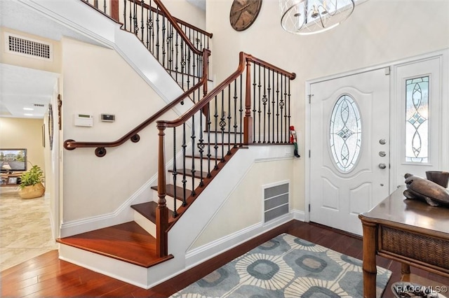 entryway featuring a chandelier, a towering ceiling, and dark wood-type flooring