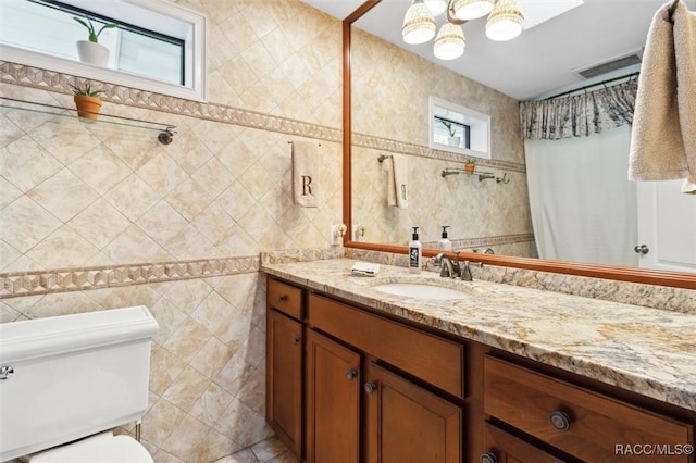 bathroom featuring vanity, toilet, and tile walls