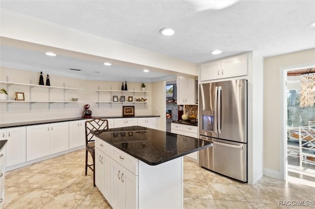 kitchen with white cabinets, a breakfast bar, stainless steel fridge, and a kitchen island