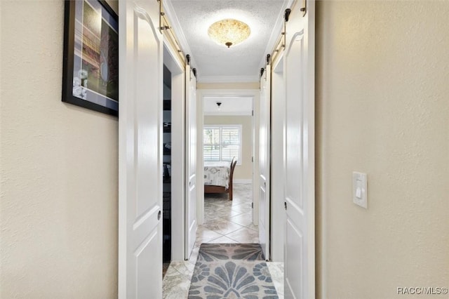 corridor with a barn door, ornamental molding, and a textured ceiling