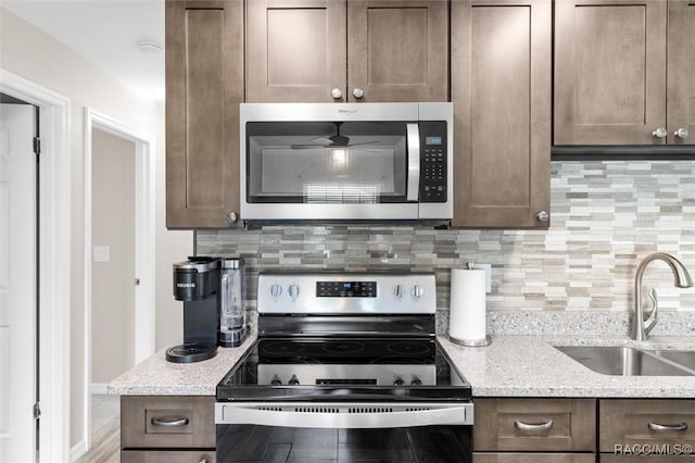 kitchen with sink, dark brown cabinets, stainless steel appliances, light stone countertops, and decorative backsplash