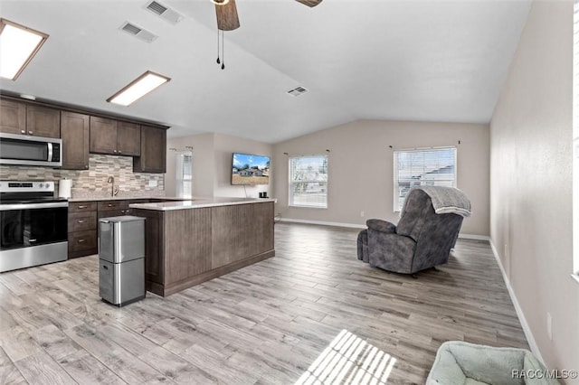 kitchen featuring tasteful backsplash, lofted ceiling, dark brown cabinetry, stainless steel appliances, and light wood-type flooring