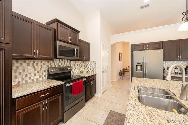 kitchen featuring arched walkways, light tile patterned floors, stainless steel appliances, a sink, and dark brown cabinets