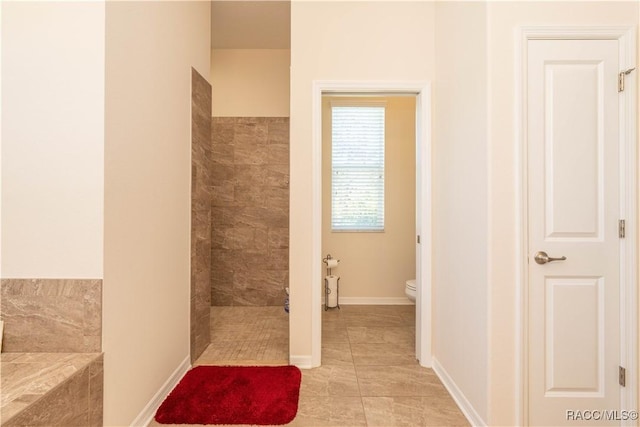 full bath featuring tile patterned flooring, a tile shower, toilet, and baseboards