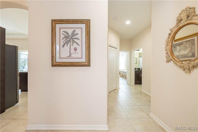 hall with a healthy amount of sunlight, light tile patterned floors, baseboards, and arched walkways